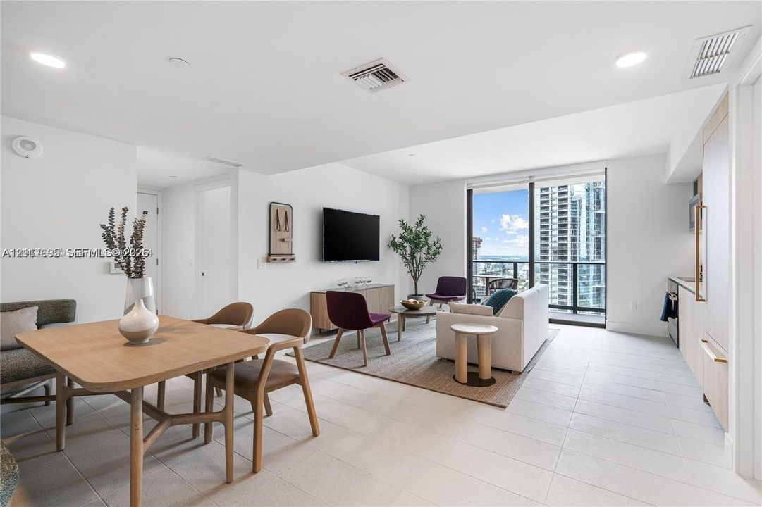 Open-concept living space featuring large-format tile flooring, floor-to-ceiling windows with access to a balcony, recessed lighting, and built-in cabinetry with integrated appliances