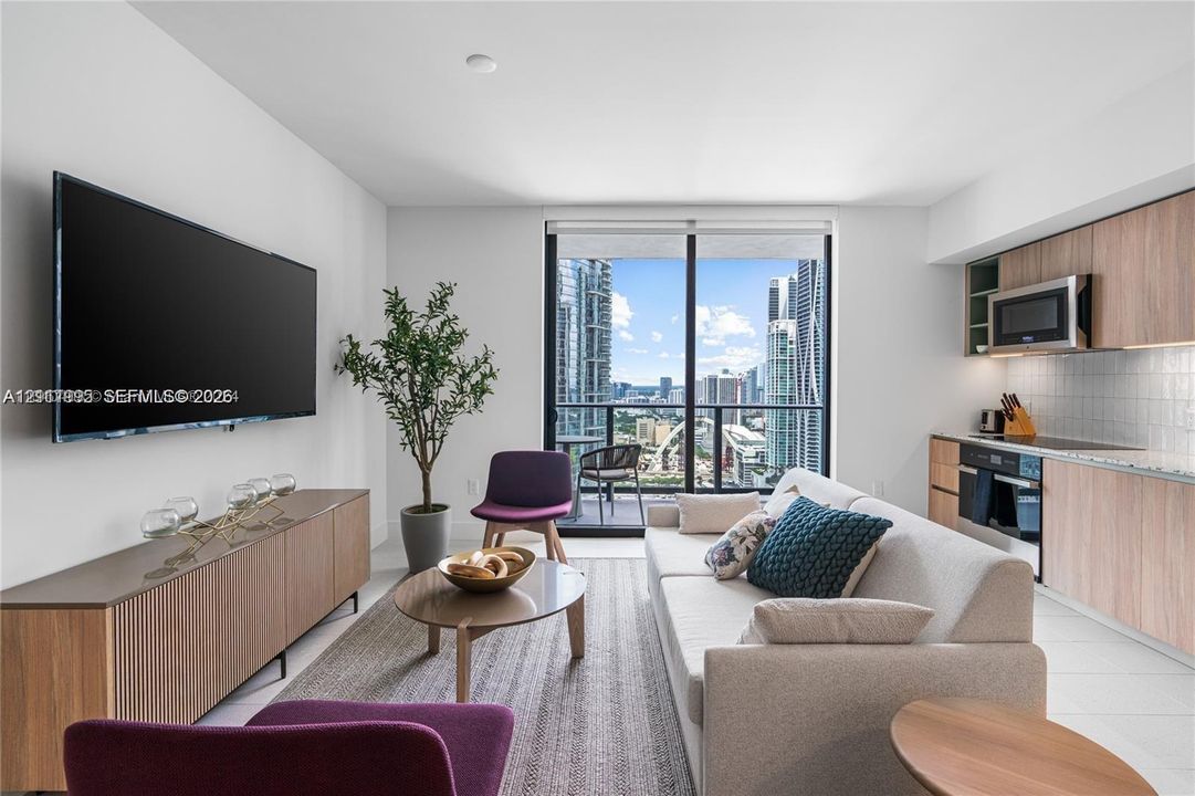 Open-concept space featuring floor-to-ceiling glass doors, private balcony, wood-finish cabinetry, and neutral tile flooring