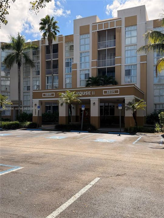 Multi-story stucco exterior featuring a covered entryway, integrated private balconies, large vertical window banks, and mature palm landscaping