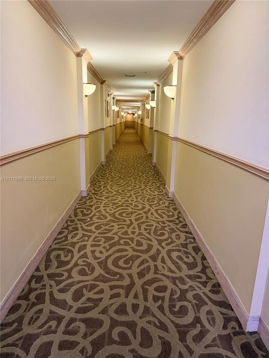 Hallway featuring patterned carpet, chair rail molding, and wall-mounted sconces