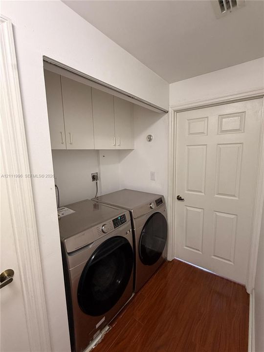 Laundry area featuring wood-finish flooring, white upper cabinetry, and a six-panel interior door