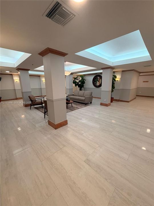 Expansive lobby featuring large-format tile flooring, recessed coffered ceilings, integrated perimeter lighting, and structural columns with wood-finish crown molding