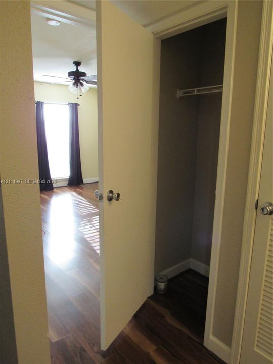 Interior space featuring wood-finish flooring, a built-in closet with overhead shelving, and a ceiling fan with integrated lighting