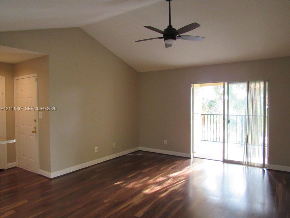 Interior space featuring vaulted ceilings, wood-finish flooring, a ceiling fan, and sliding glass doors with access to an exterior balcony