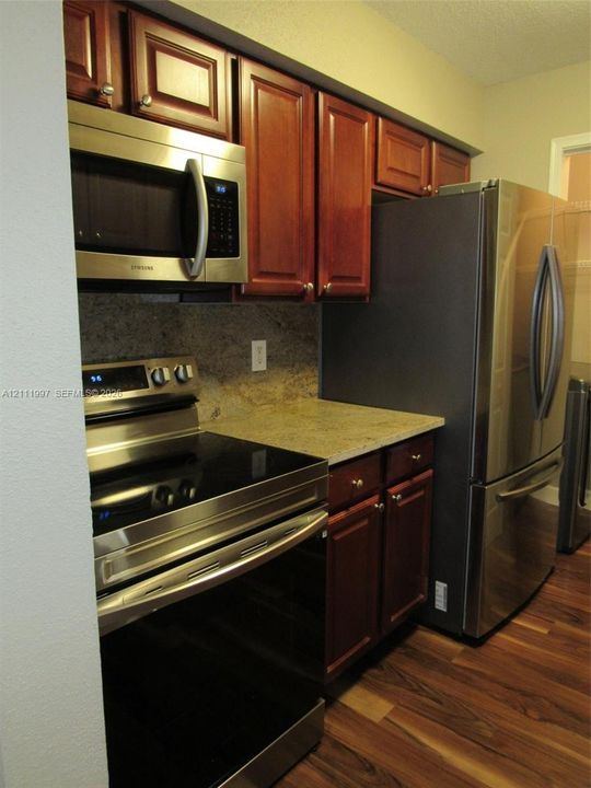 Kitchen featuring dark-toned wooden cabinetry, stone countertops, stainless steel appliances, and wood-finish flooring