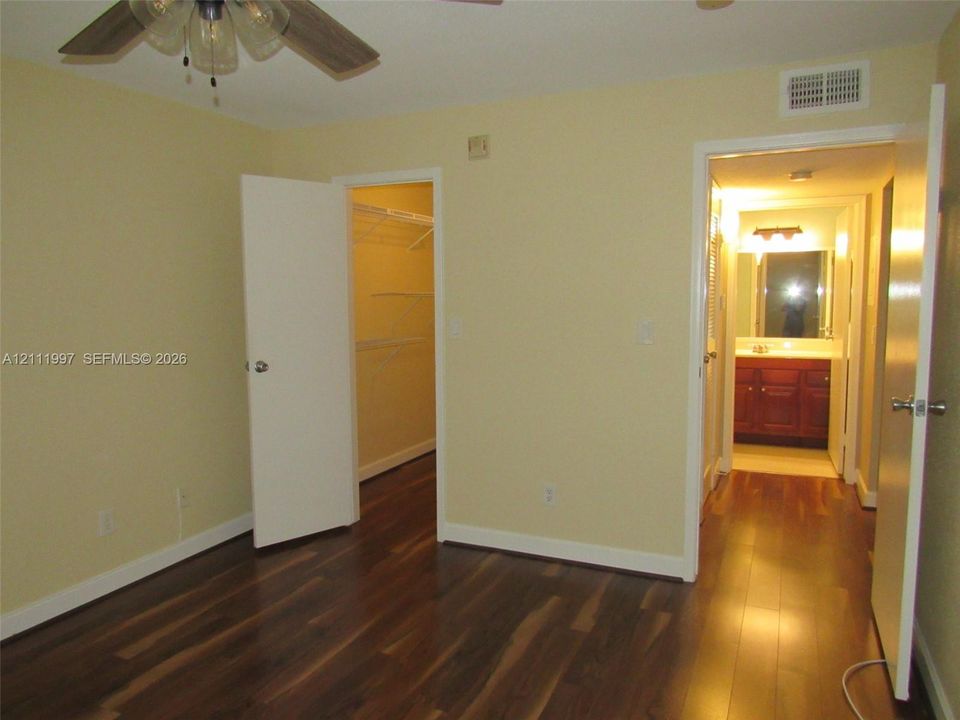 Wood-finish flooring, ceiling fan with integrated light fixture, walk-in closet with wire shelving, and bathroom featuring vanity cabinetry
