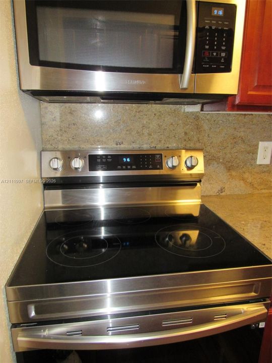 Stainless steel over-the-range microwave and electric range with a glass cooktop, paired with a solid-surface backsplash and countertop