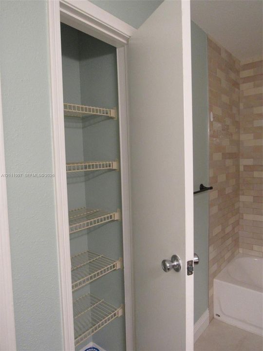 Built-in storage closet featuring five wire shelving tiers, complemented by a matte black towel bar and textured stone-finish wall tile surrounding the bathtub