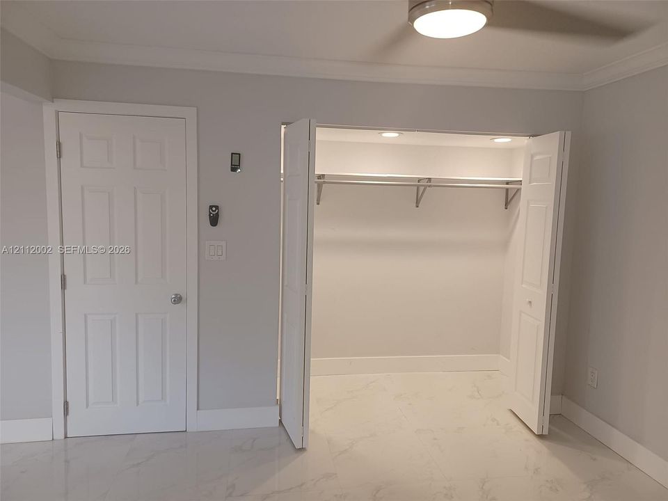 Walk-in closet featuring built-in shelving and recessed lighting, paired with polished stone-finish flooring and a white paneled door