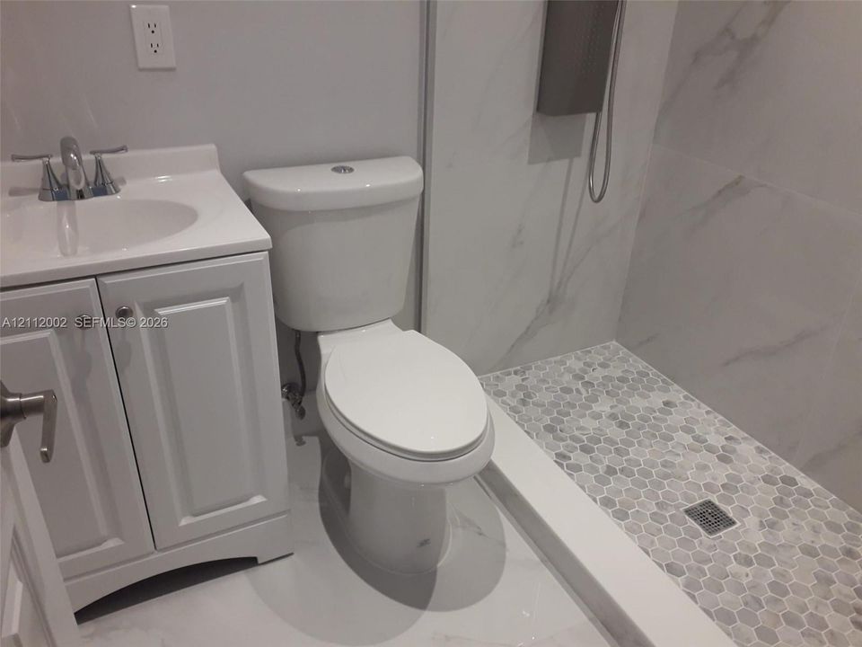 Bathroom featuring a white vanity cabinet with a integrated sink, two-piece toilet, and a walk-in shower with large-format wall tile and a hexagonal tile floor