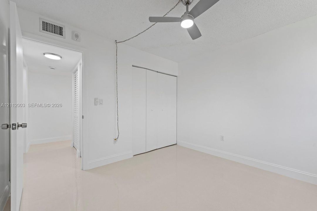 Neutral-toned tile flooring, white-finish walls, ceiling-mounted light fixture with fan, and bi-fold closet doors