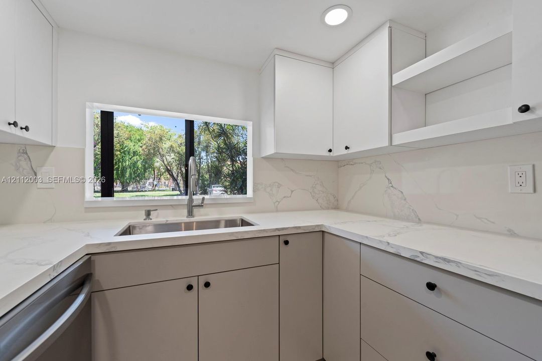 Kitchen featuring custom flat-panel cabinetry, stone-patterned countertops, a full-height stone-patterned backsplash, undermount stainless steel sink with high-arc faucet, and open display shelving
