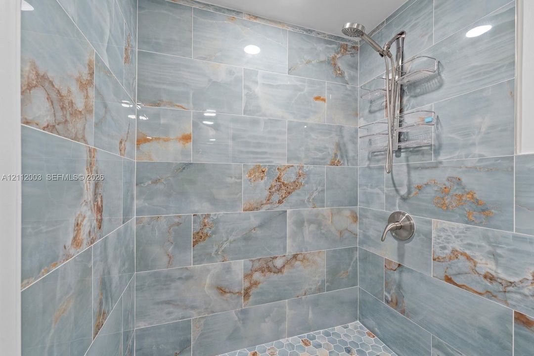 Shower stall featuring large-format, blue and gold veined tile surround, hexagonal tile floor, and polished chrome fixtures