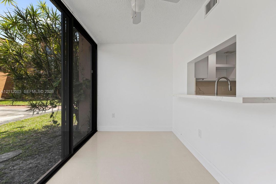 Floor-to-ceiling sliding glass door, white ceramic tile flooring, and pass-through counter with a stone-finish surface and metal faucet