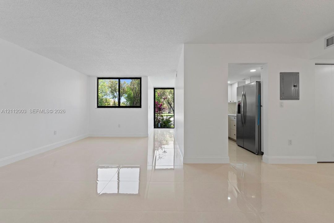 Open-concept interior featuring large-format polished tile flooring, neutral wall finishes, black-trimmed window frames, and stainless steel kitchen appliances