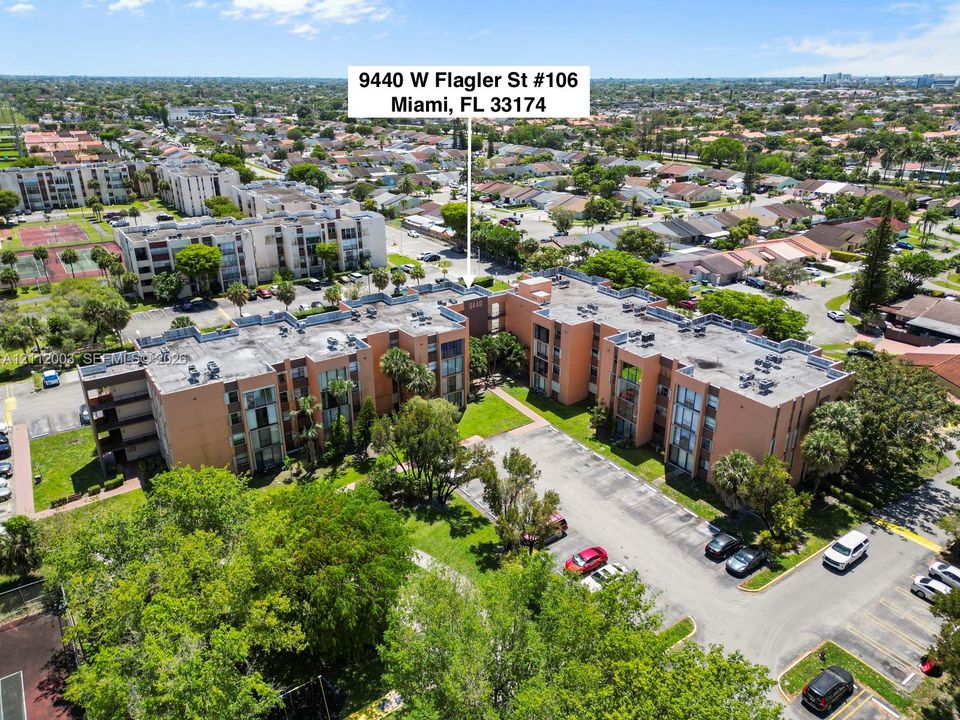 Aerial perspective of a multi-story residential building featuring masonry exterior construction, flat roof design, surface-level parking, and mature trees