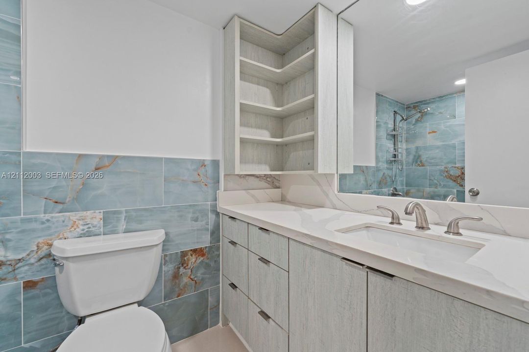 Vanity featuring light-toned cabinetry, built-in corner shelving, integrated countertop with rectangular basin, and blue-toned tile wall treatments