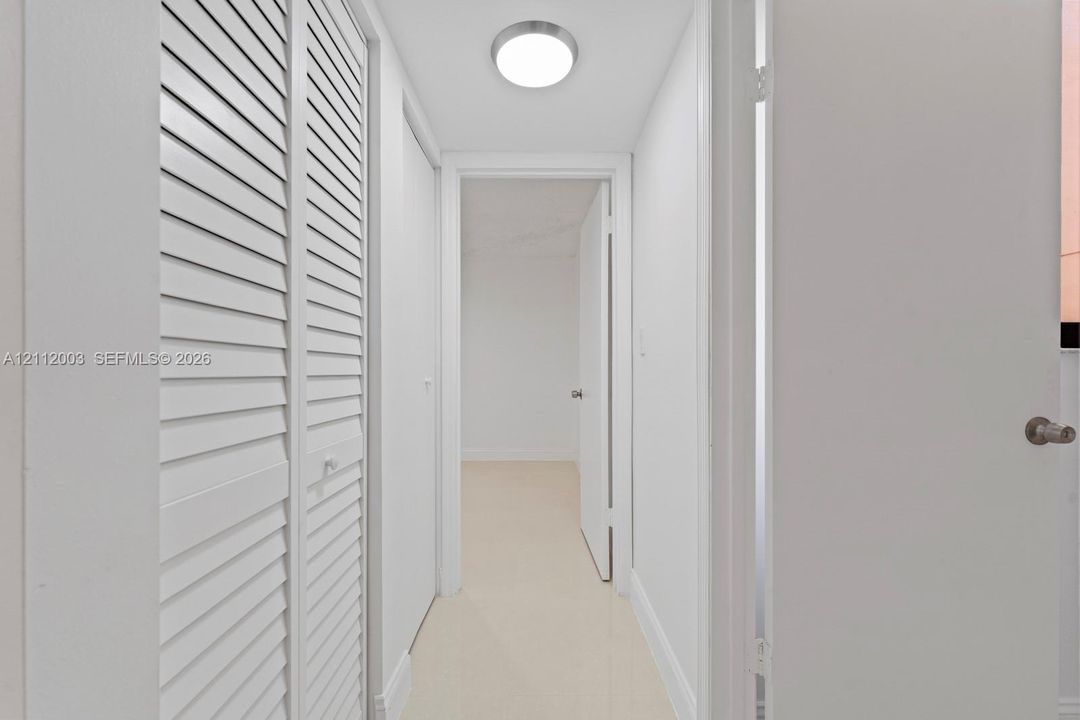 Interior hallway featuring white louvered closet doors, neutral-toned flooring, and a flush-mount circular ceiling light
