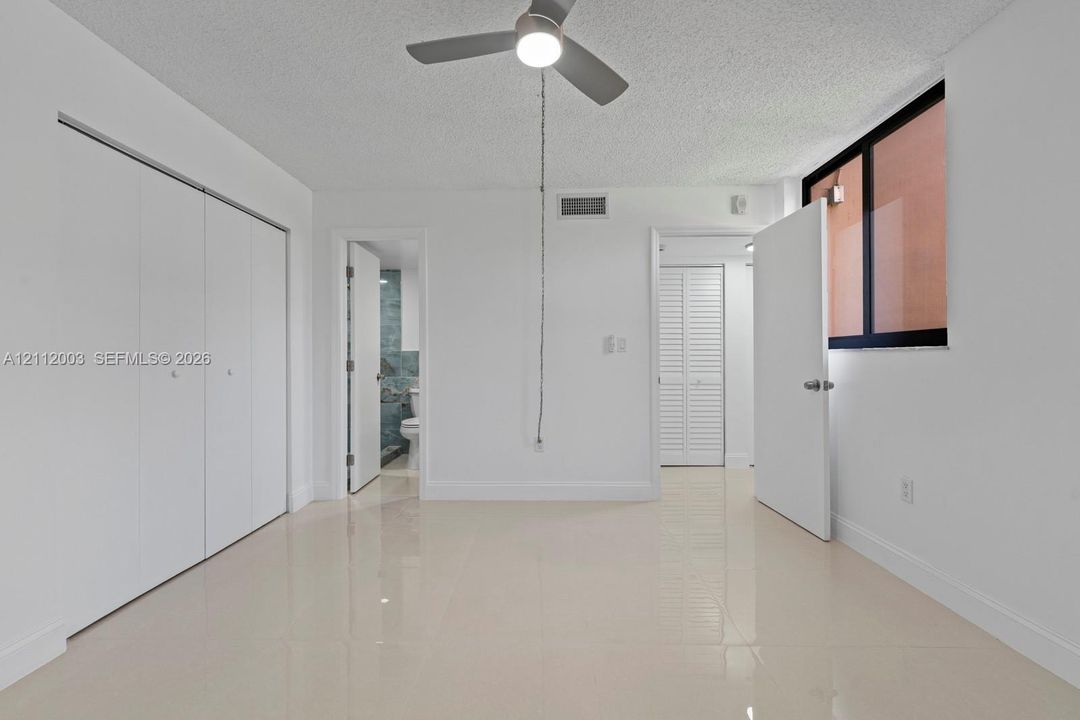 Interior room featuring polished tile flooring, white bi-fold closet doors, a ceiling fan with integrated lighting, and a window with a dark frame