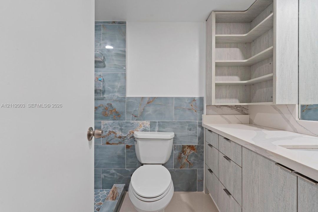Bathroom featuring a wood-finish vanity with a stone-top counter, blue-toned tile wall accents, and custom built-in shelving