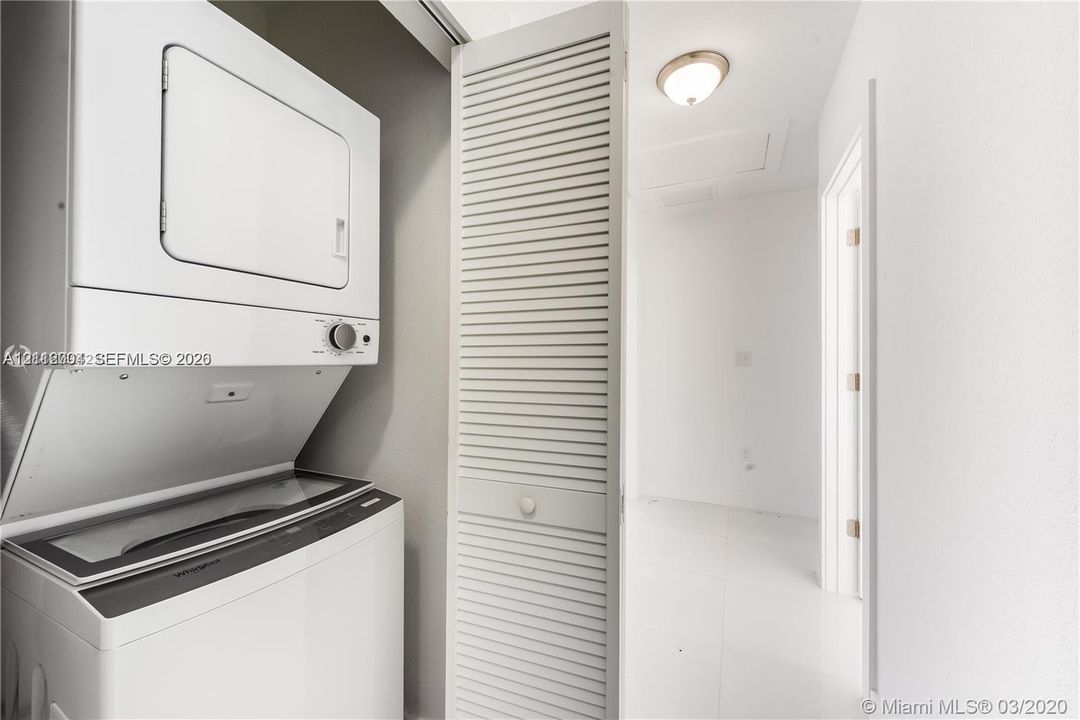 Stacked laundry unit enclosed by a white louvered door featuring a circular knob and a ceiling-mounted dome light fixture