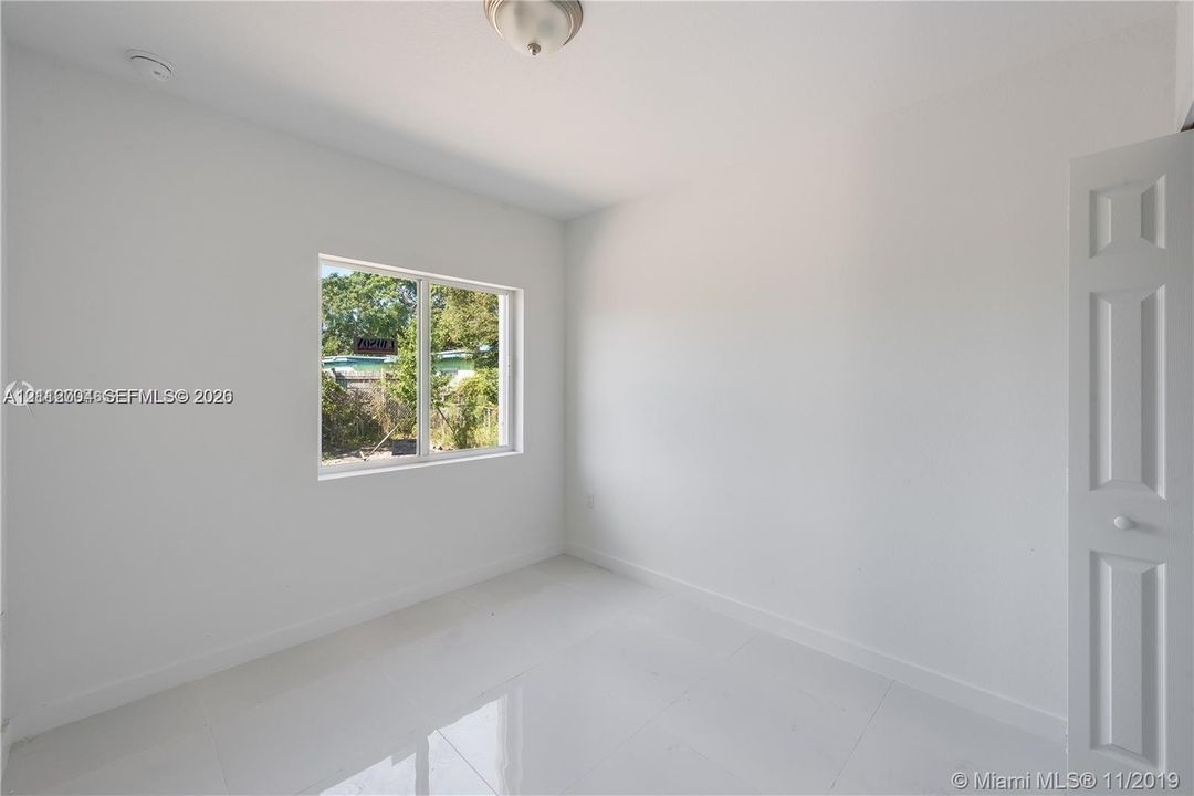Interior space featuring polished tile flooring, white walls, a single-pane window, and a multi-panel interior door