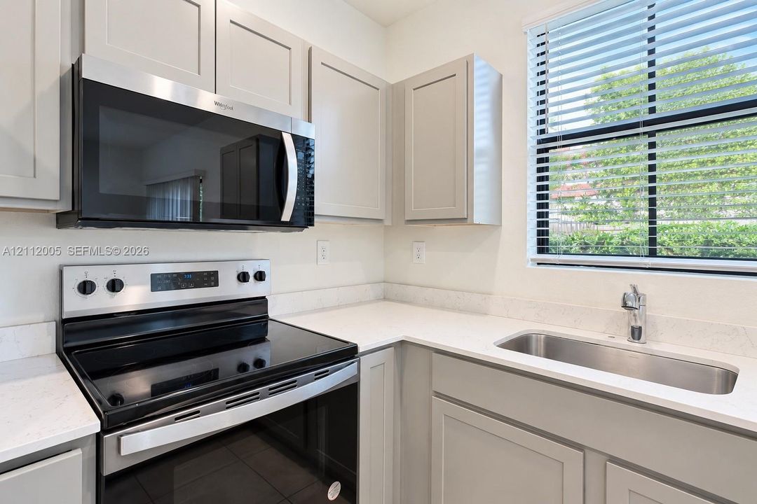 Kitchen featuring light-toned shaker cabinetry, stone-finish countertops, stainless steel undermount sink, integrated stainless steel appliances, and horizontal window blinds