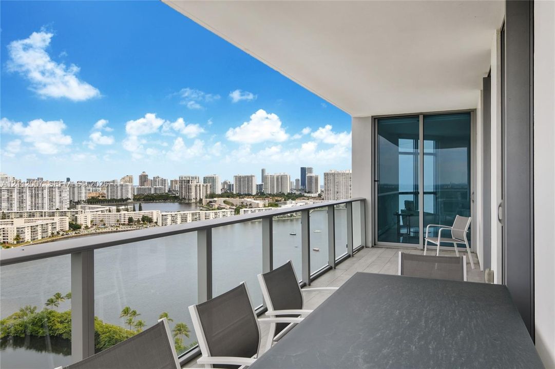 Covered balcony with a glass panel railing, tile flooring, and floor-to-ceiling sliding glass doors