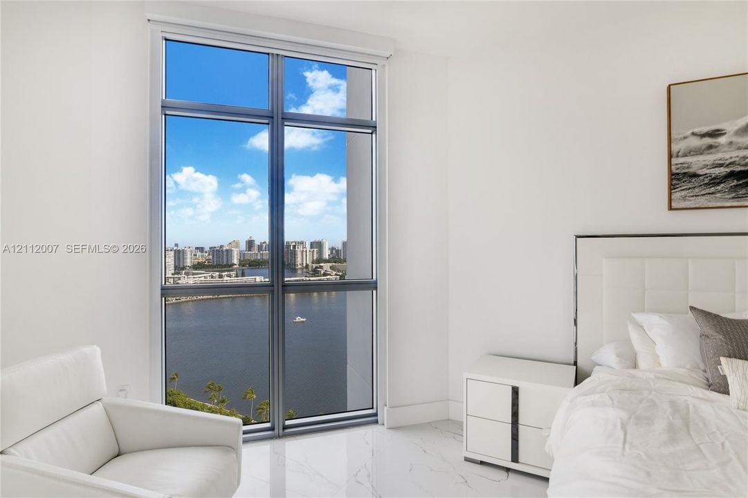 Floor-to-ceiling windows featuring panoramic water and cityscape scenery, complemented by light-toned stone flooring