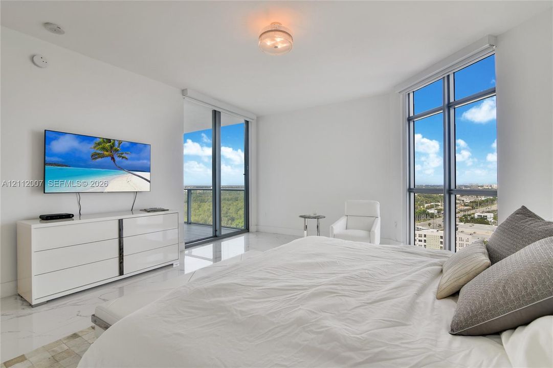 Floor-to-ceiling windows, polished stone-finish flooring, and a sliding glass door providing access to an exterior balcony