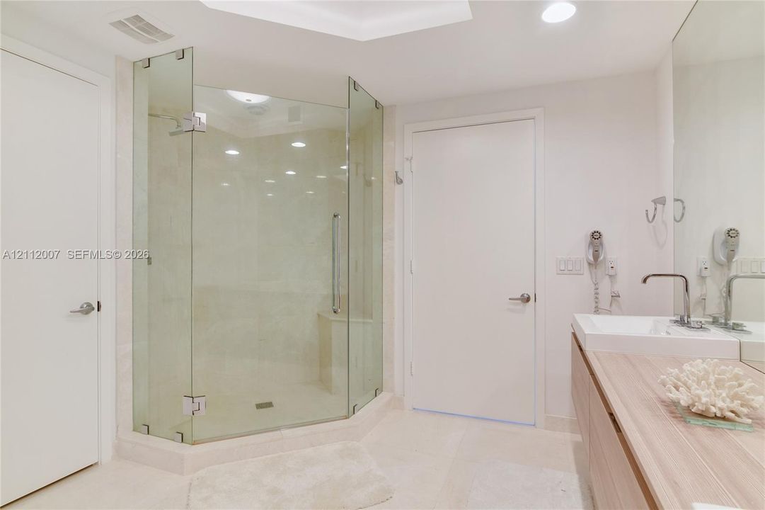 Glass-enclosed corner shower with built-in bench, wall-mounted vanity with wood-finish cabinetry, rectangular vessel sink, and wide-format tile flooring