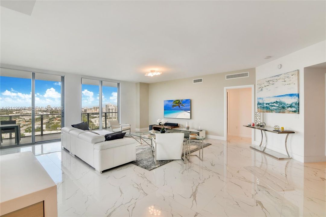 Open-concept interior featuring large-format stone-finish flooring, floor-to-ceiling glass sliding doors, and private balcony access