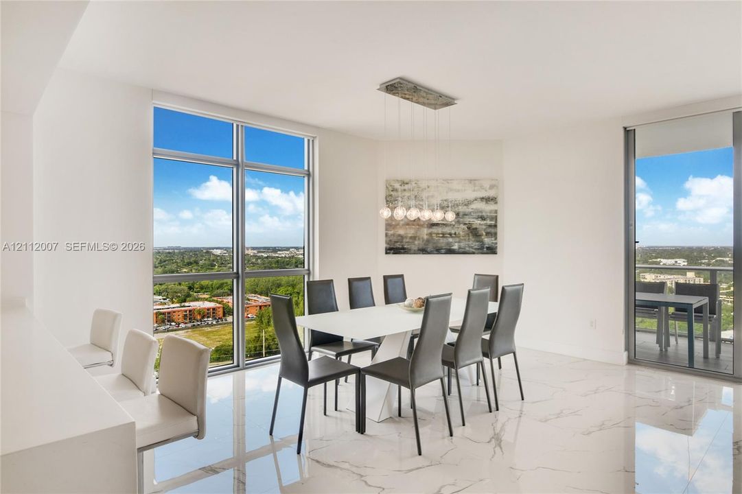 Dining area featuring floor-to-ceiling windows, polished stone-finish tile flooring, a linear multi-bulb pendant light fixture, and a glass-paneled sliding door leading to a balcony