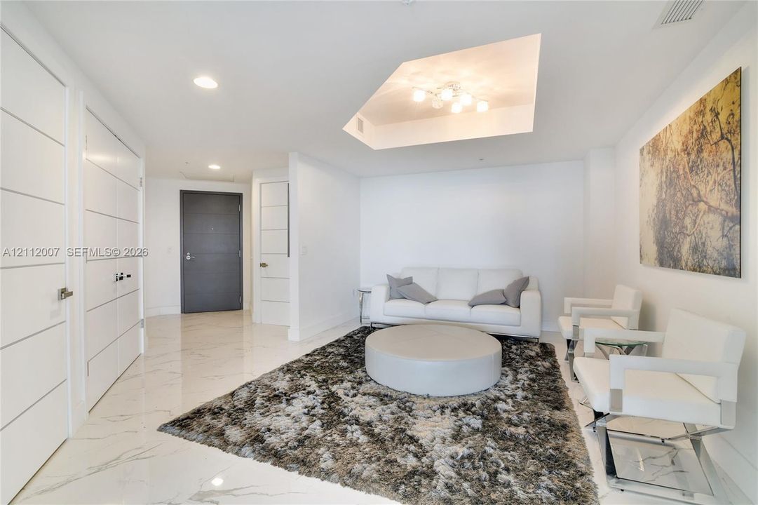 Interior space featuring polished stone-finish flooring, a recessed tray ceiling with multi-bulb architectural lighting, and modern multi-panel interior doors