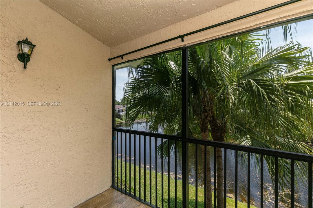 Covered porch featuring wood-finish flooring, stucco walls, attached exterior wall-mounted lighting, and a screened-in enclosure with metal railings