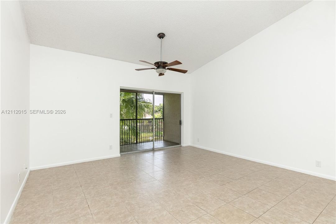Room featuring vaulted ceilings, tile flooring, a central ceiling fan, and sliding glass doors with access to a railed balcony