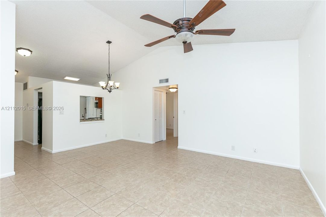 Vaulted ceilings featuring a central ceiling fan, neutral tile flooring, a decorative chandelier, and a kitchen pass-through window