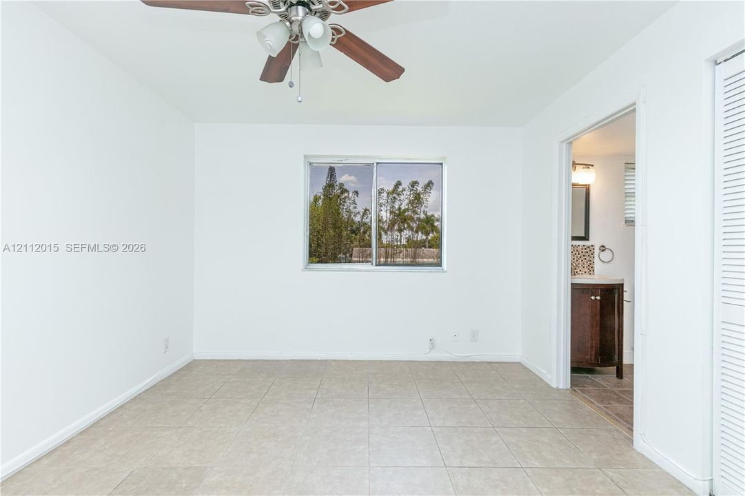 Room featuring neutral tile flooring, a central ceiling fan with integrated lighting, a sliding window, and a louvered closet door