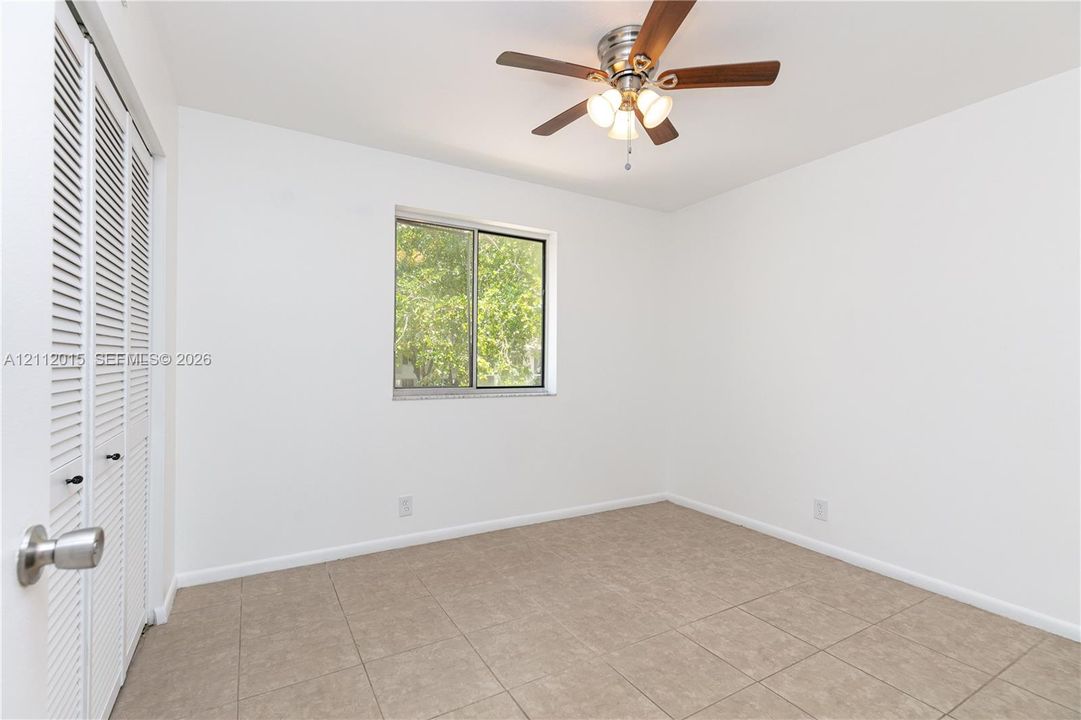 Room featuring tile flooring, ceiling fan with integrated lighting, window, and bifold closet doors