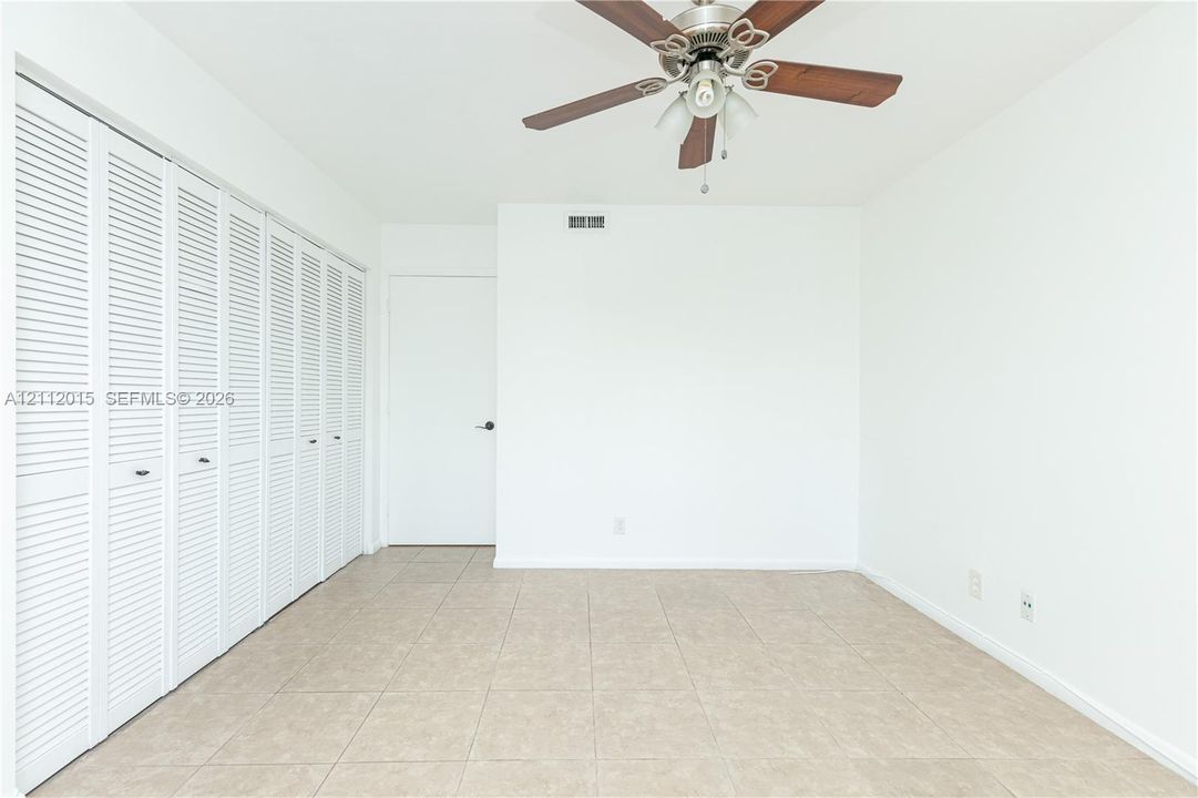 Neutral-toned ceramic tile flooring, multi-panel louvered closet doors, and a ceiling-mounted fan with integrated lighting