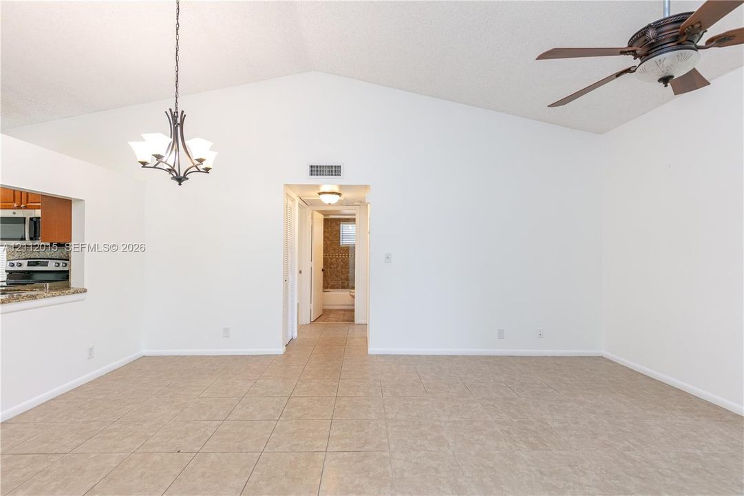 Vaulted ceiling featuring a central multi-light chandelier and a multi-blade ceiling fan, finished with ceramic tile flooring