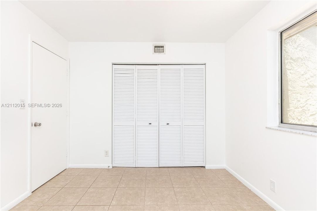 Neutral interior space featuring tile flooring, a multi-panel closet with louvered doors, a solid-panel door, and a window with a stone sill