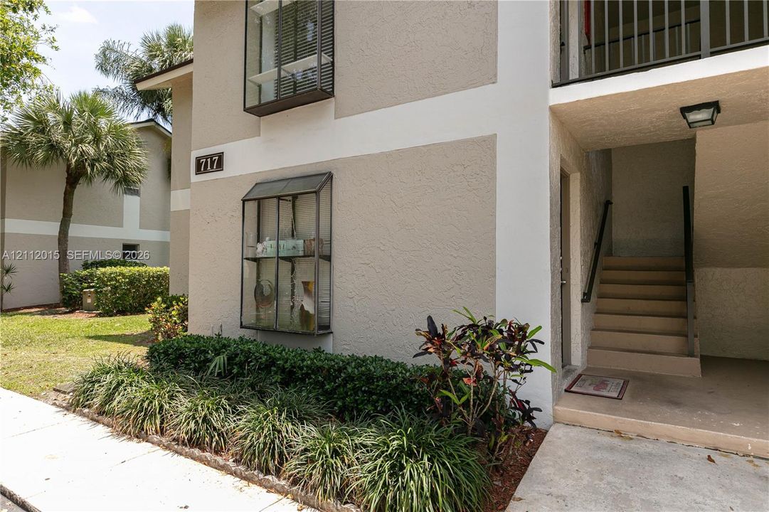 Stucco exterior featuring dual-level window boxes, concrete stairs with metal handrails, and low-maintenance landscaping