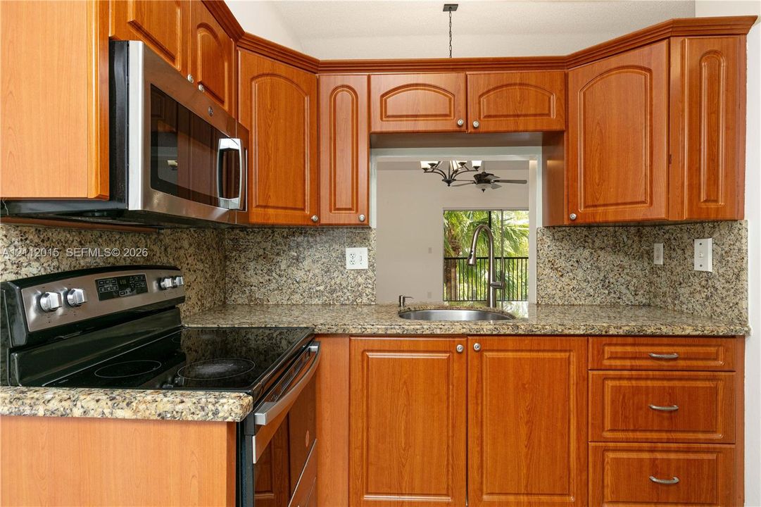 Kitchen featuring warm-tone wood cabinetry, stone countertops, stainless steel electric range, built-in microwave, and an undermount sink
