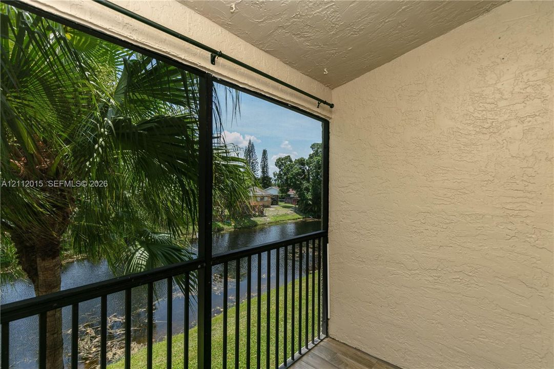 Screened-in balcony featuring black metal railings, textured stucco walls, and tile flooring
