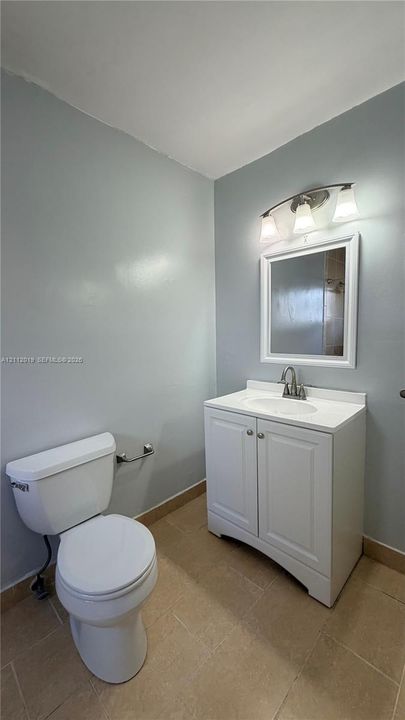 Bathroom featuring a white vanity cabinet with a stone-top surface, integrated sink, three-light fixture, and ceramic tile flooring