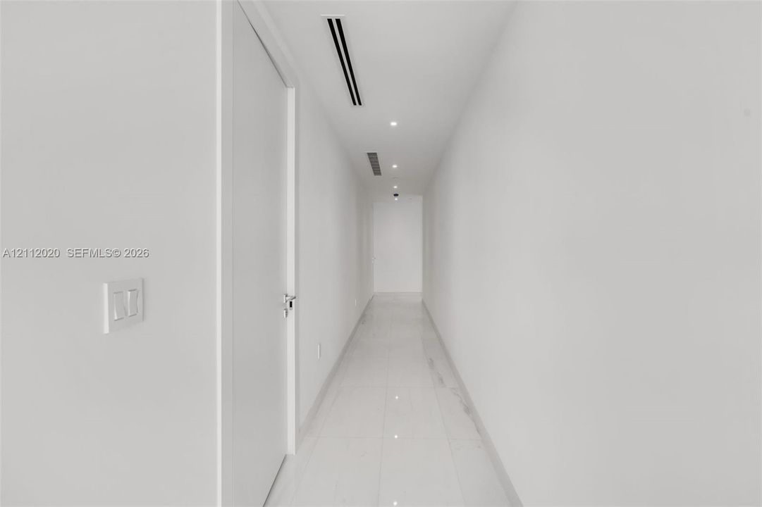 Minimalist hallway featuring white tile flooring, flush-mount recessed lighting, and integrated linear ceiling components