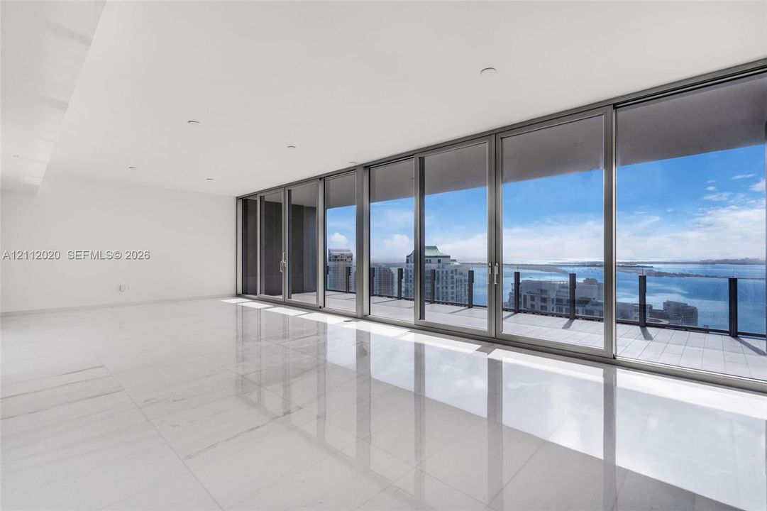 Floor-to-ceiling sliding glass doors, expansive private terrace with glass railing, large-format polished tile flooring, recessed ceiling lighting, and panoramic water and city scenery