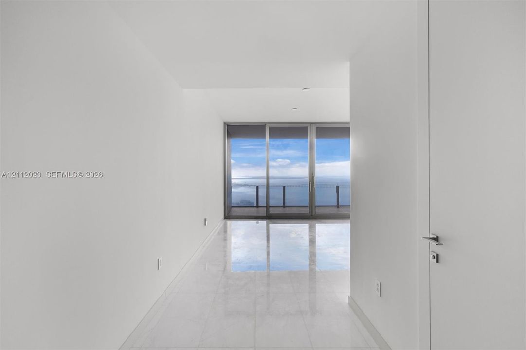 Minimalist interior featuring large-format stone flooring, floor-to-ceiling glass sliding doors, and a private balcony with water scenery