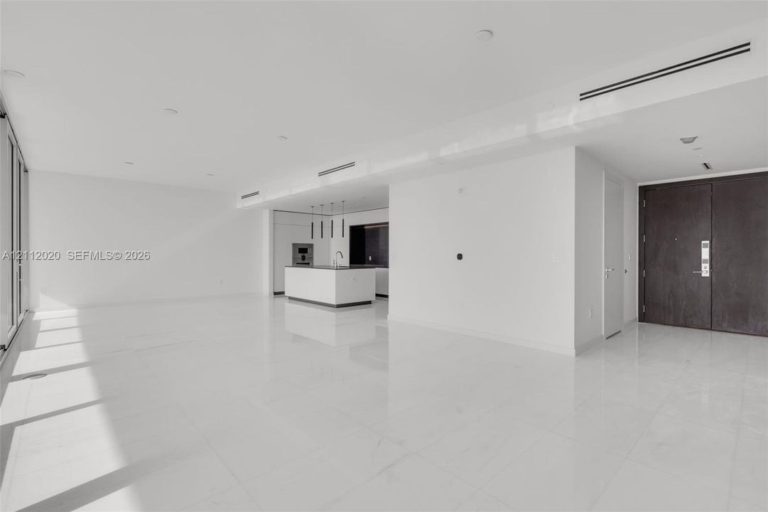 Open-concept interior featuring large-format tile flooring, recessed ceiling lighting, linear air diffusers, a kitchen island with built-in cabinetry, and a dark-finish double-door entry